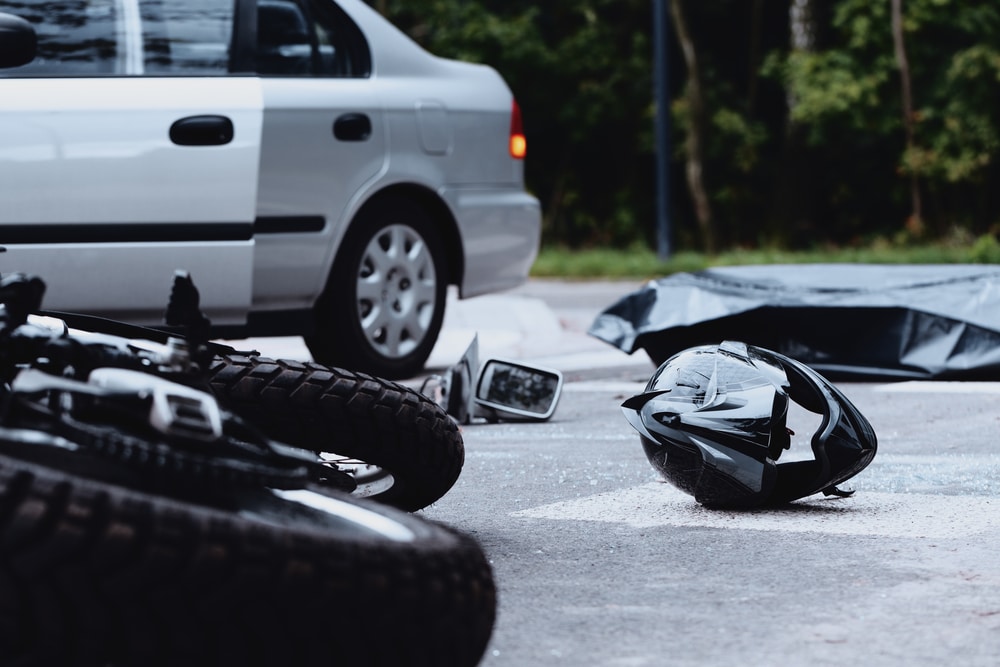 Motorcycle and helmet on street after crash car in background